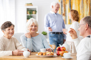 Lächelnde Personen sitzen oder stehen am Tisch mit Kuchen und Kaffee